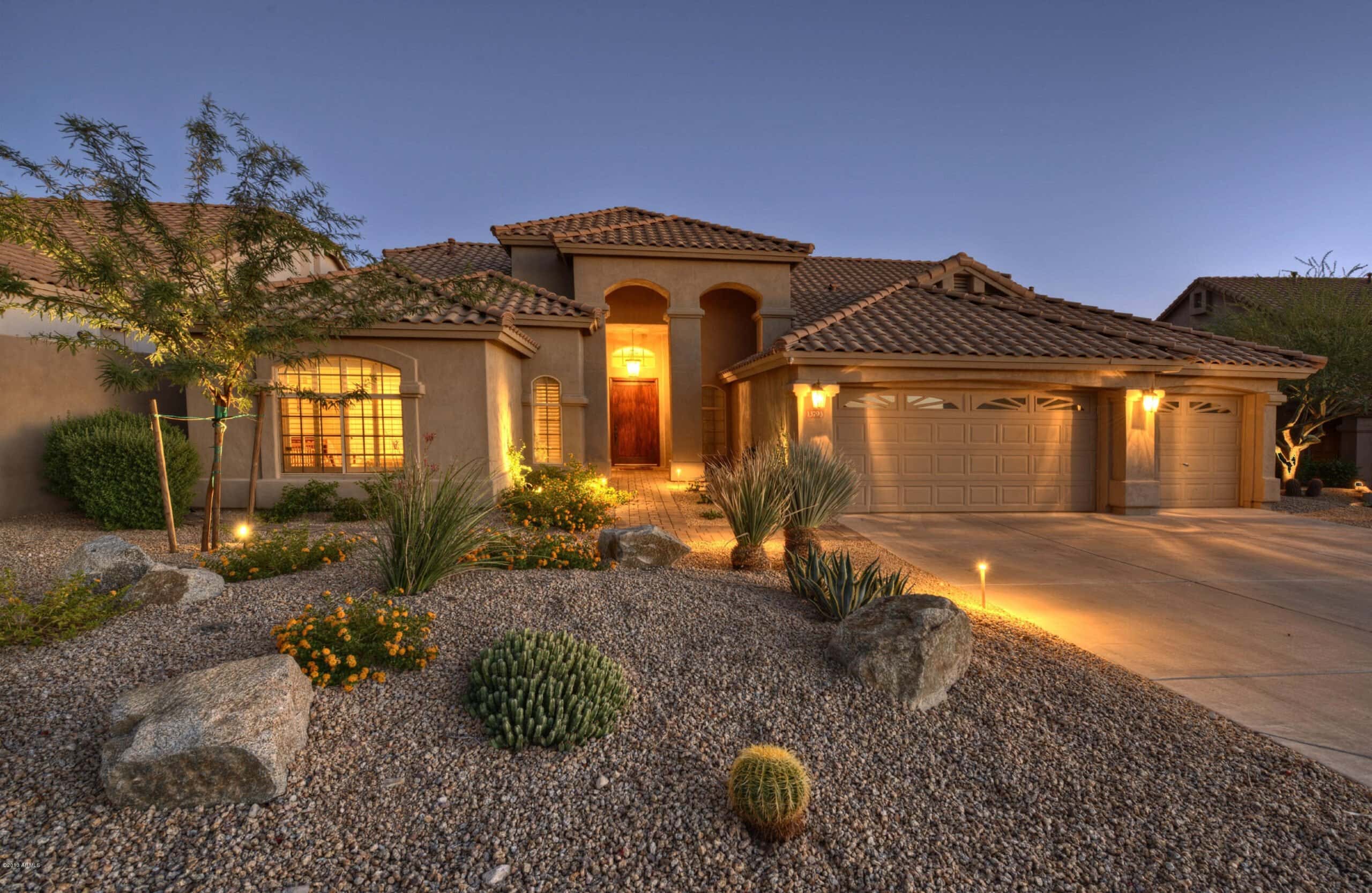 A lit-up Arizona home at dusk with desert landscaping